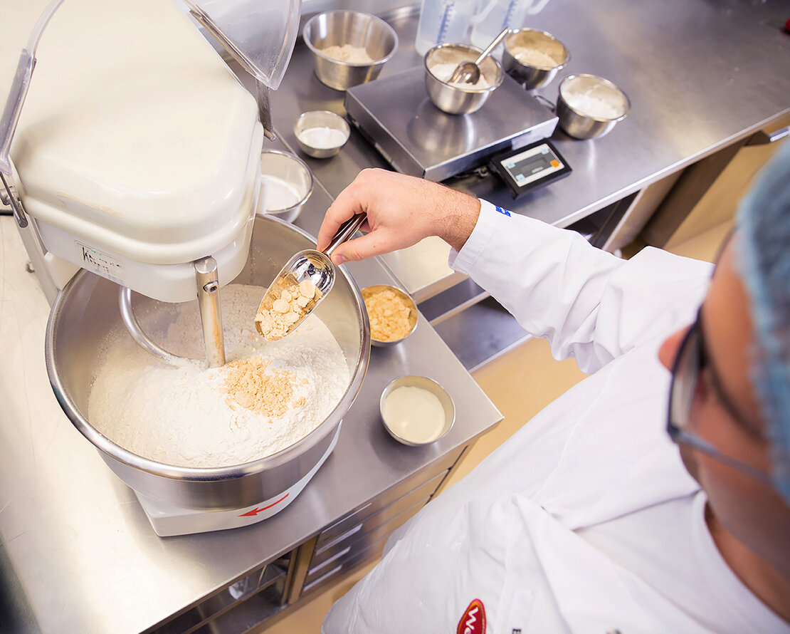 Picture of an employee of Wewalka, adding varous ingredients in a mixer to develop a new fresh dough recipe