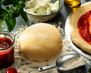 Picture of a Wewalka sourdough-ball, on a kitchen worktop, already shown with tomato sauce with other ingredients like basil, mozzarella, fresh tomatoes and grilled vegetables